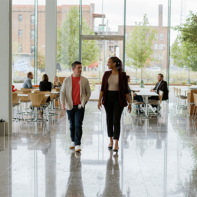 Two individuals walking down a hallway and talking
