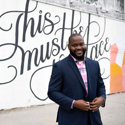 an individual in a suit standing in front of a mural