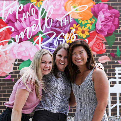a group of three people in front of a floral mural