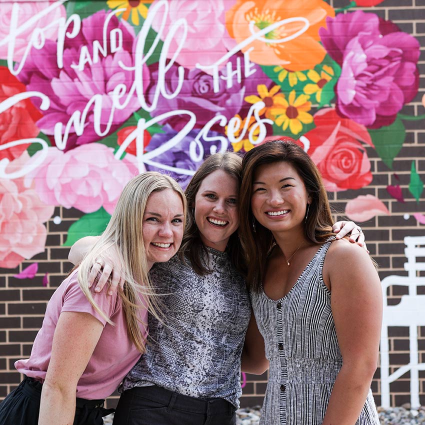 a group of three people in front of a floral mural