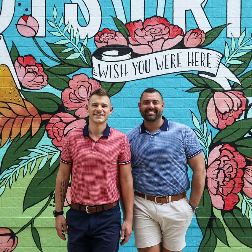 two people standing in front of a mural that says wish you were here