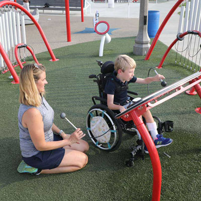 a child in a wheelchair plays while an adult looks on