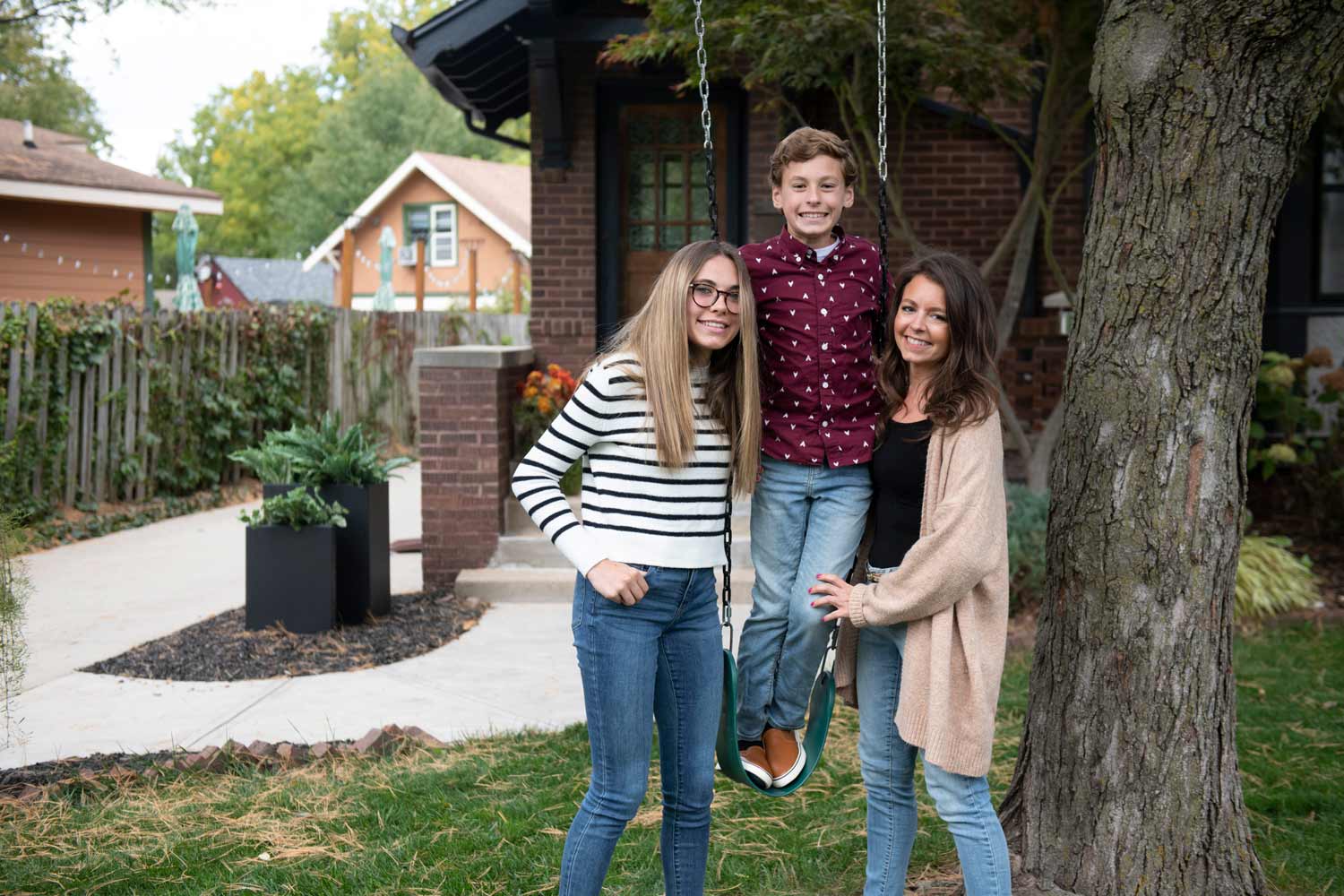 A family smiling for a photo on a swing in front of a home.