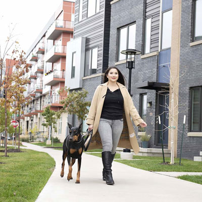 a young woman walking a dog with townhomes and apartments behind her.