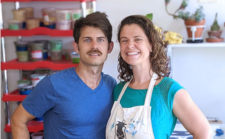 A male and female smiling for a photo in front of paints
