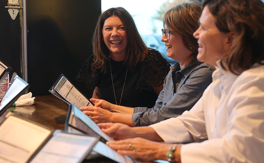 Three women laughing at a table with menus in their hands