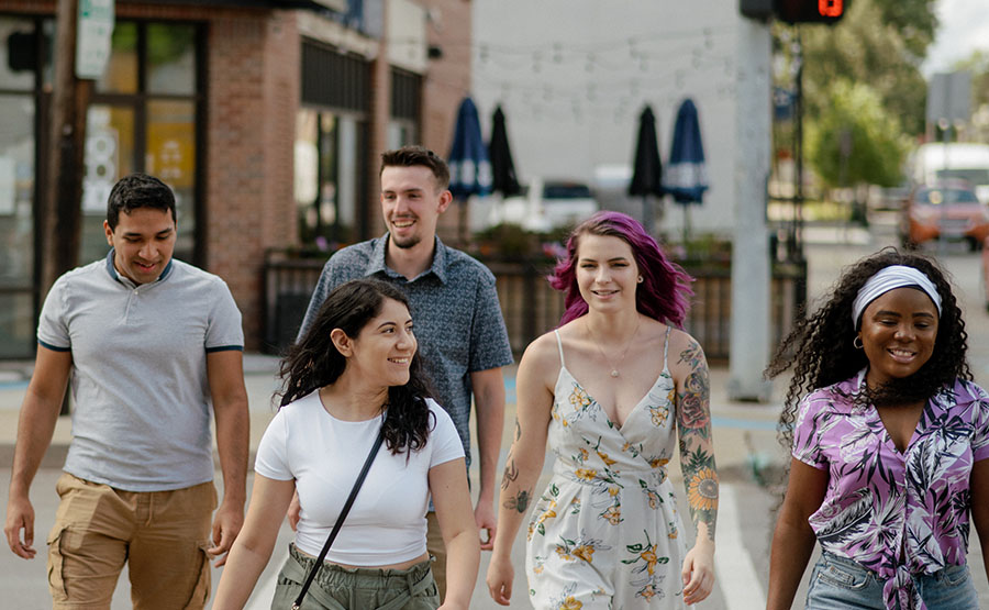 Five young adults laughing and talking as they walk acr