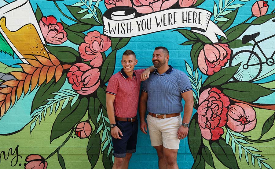 Two men smiling together in front of a mural