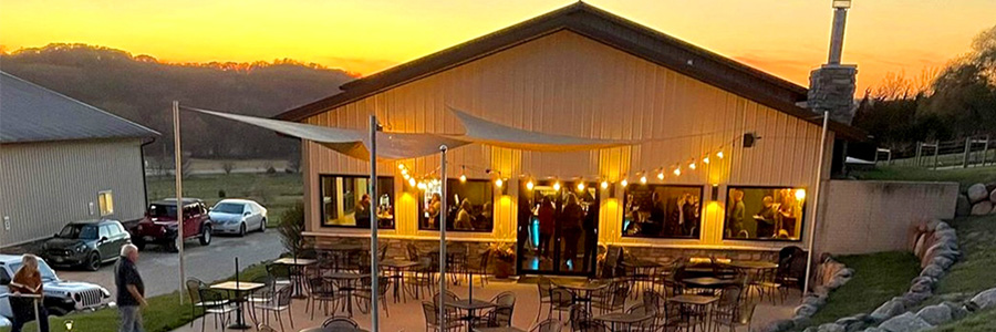 A patio in front of a building with chairs tables, and lights. The sun is setting behind the building.