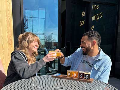 two people with a flight of beer and cheersing their drinks. 