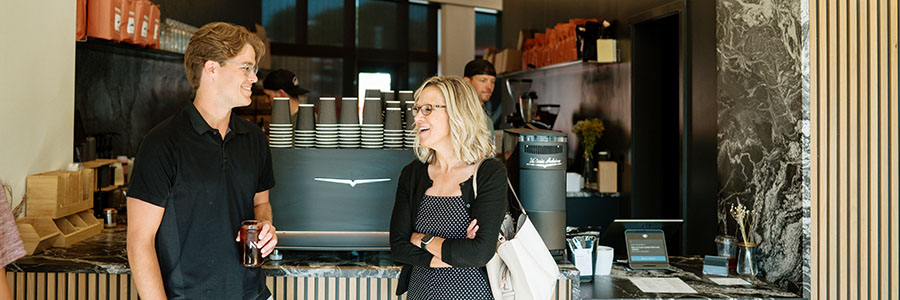 Two people standing in front of an espresso bar talking and laughing