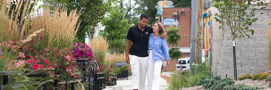 a couple walking down a sidewalk with plants and greenery along the path.