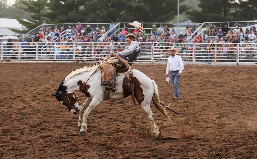 A cowboy riding a horse in a dirt arena. He is holding 