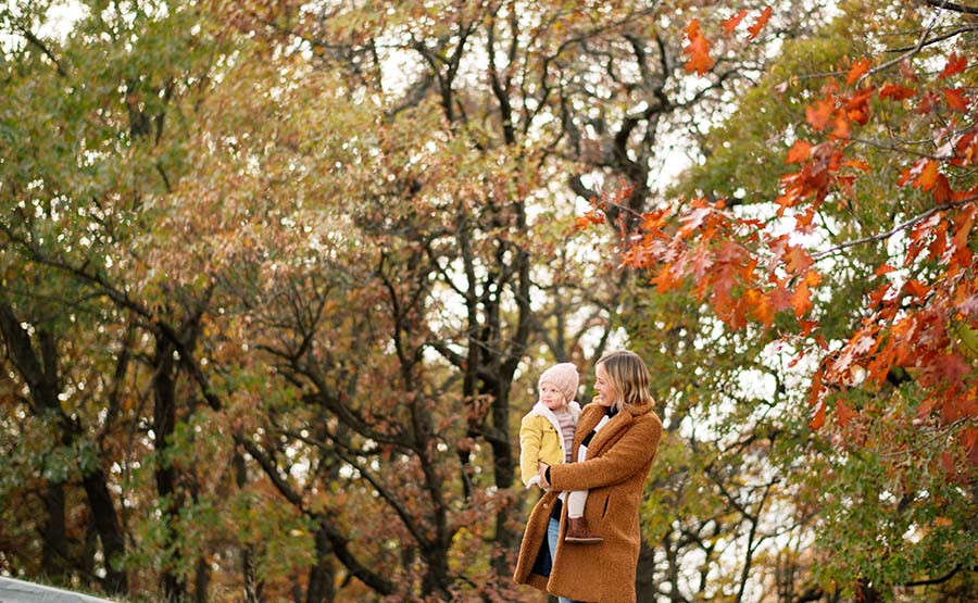 A woman holding a child surrounded by the autumn trees 