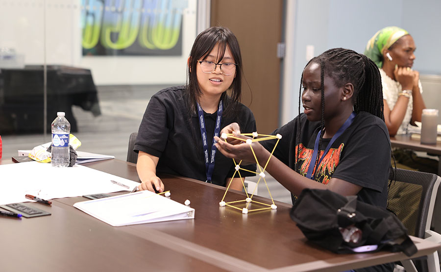 Two students building a structure with dried noodles an