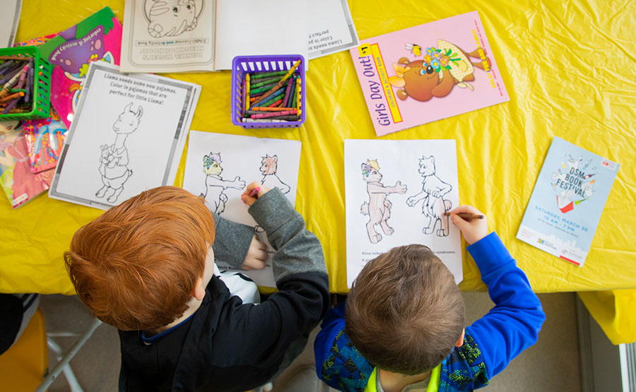 An overhead view of two children coloring on paper.