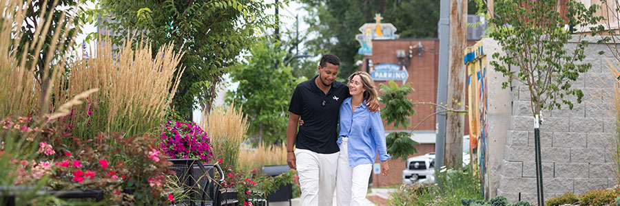 A couple walking down a side walk, smiling together.