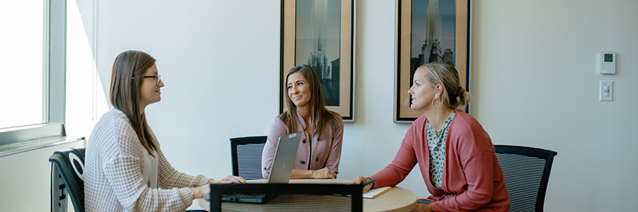 Three women gathered around a table having a meeting.