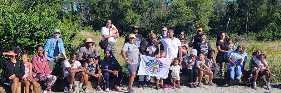 Black Iowa Outdoors A group of people, smiling for a photo and holding up a banner that says Black Iowa Outdoors