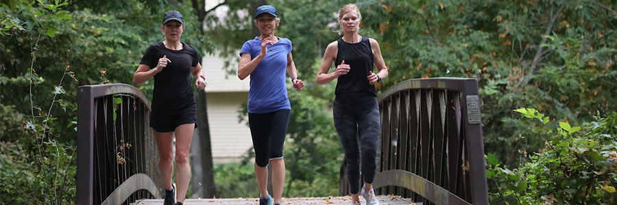 three adults running over a paved bridge that is surrounded by greenery