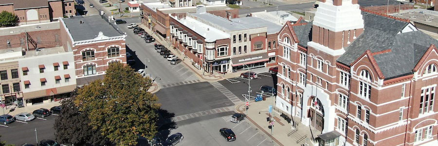 High view of part of the Oskaloosa Town Square. The buildings are mainly brick and there are several cars parked along the side of the road.
