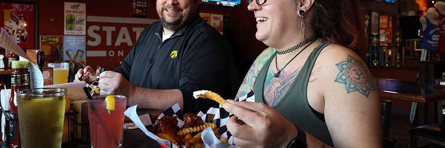 The Station Two people enjoying wings and fries. Both are laughing.