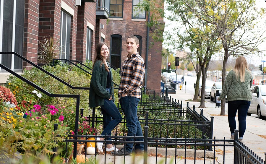 A young couple smiling on the steps of a brick town hom